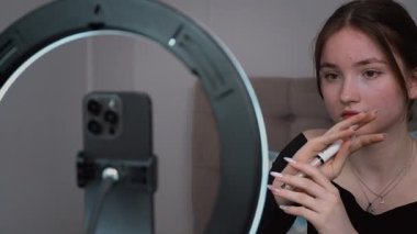 Genç vlogger çocuk kanalı için video blogu yapıyor. Güzellik blogları, teknoloji ve insan konsepti. Yüzük ışığı ve akıllı telefonla evde makyaj yapan mutlu gülümseyen kız blogcu.