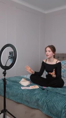 Genç vlogger çocuk kanalı için video blogu yapıyor. Güzellik blogları, teknoloji ve insanlar konsepti - mutlu gülümseyen kız blogcu, zil ışığı ve akıllı telefon ile evde dikey video uygulaması