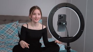 Genç vlogger çocuk kanalı için video blogu yapıyor. Güzellik blogları, teknoloji ve insan konsepti. Yüzük ışığı ve akıllı telefonla evde makyaj yapan mutlu gülümseyen kız blogcu.