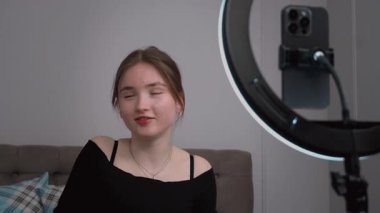 Genç vlogger çocuk kanalı için video blogu yapıyor. Güzellik blogları, teknoloji ve insan konsepti. Yüzük ışığı ve akıllı telefonla evde makyaj yapan mutlu gülümseyen kız blogcu.