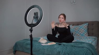 Güzel kız genç profesyonel blogger makyaj sanatçısı kozmetik inceleme ürünlerini canlı video vlog kanalı genç kız video kaydı için gösteriyor. Akıllı telefonundan. Yüzük lambasıyla aydınlatma.