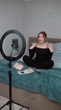 Güzel kız genç profesyonel blogger makyaj sanatçısı kozmetik inceleme ürünlerini canlı video vlog kanalı genç kız video kaydı için gösteriyor. Akıllı telefonundan. Yüzük lambasıyla aydınlatma.