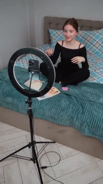 Güzel kız genç profesyonel blogger makyaj sanatçısı kozmetik inceleme ürünlerini canlı video vlog kanalı genç kız video kaydı için gösteriyor. Akıllı telefonundan. Yüzük lambasıyla aydınlatma.