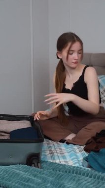 Seyahat planlayan mutlu genç kız, bavul hazırlıyor, kameraya bakıyor ve yolculuk için bavulu hazırlıyor, yatak odasında bavulunu katlıyor ve açıyor..