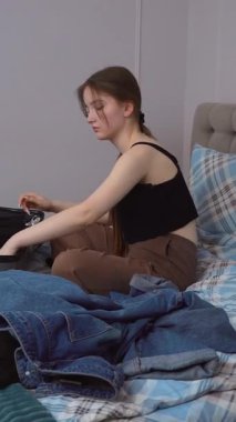 Genç bir kadın, giysilerini düzenli olarak katlıyor ve kişisel giysilerini seyahat çantasına yerleştiriyor. Yatakta oturmuş, yaklaşan dikey yolculuk videosuna hazırlanıyor.