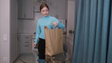 Eko-alışveriş. Kese kağıdından paketleri açan genç kız mutfak masasındaki eko torbalara organik sebzeler ve meyveler koyuyor. Süpermarketten çevrimiçi teslimat