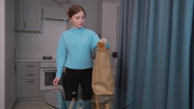 Eko-alışveriş. Kese kağıdından paketleri açan genç kız mutfak masasındaki eko torbalara organik sebzeler ve meyveler koyuyor. Süpermarketten çevrimiçi teslimat