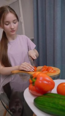 Genç kız domatesleri ahşap bir kesim tahtasında doğruyor. Etrafı marul, salatalık, dolma biber ve soğan gibi taze sebzelerle çevrili. Ev mutfağında sağlıklı bir salata hazırlıyorlar.