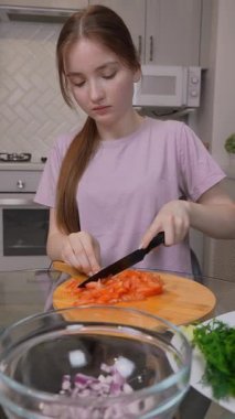 Genç Solak Genç Kız Ahşap Kesme tahtasında Taze Domatesleri Taze Dilimliyor, Besleyici Tabakları Çıtır Marul Yaprakları ve Soğanları Parlak Ev Yemeğiyle Hazırlıyor