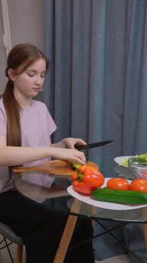 Genç kız, domates, biber ve marul gibi taze sebzelerle çevrili ahşap kesim tahtasının üzerinde salatalık doğruyor.