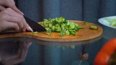 Profesyonel kadın şef, ahşap kesme tahtasıyla taze salatalıkları dikkatlice dilimliyor. Mutfak ortamında mükemmel pişirme tekniğiyle parlak sağlıklı bir salata hazırlıyor.