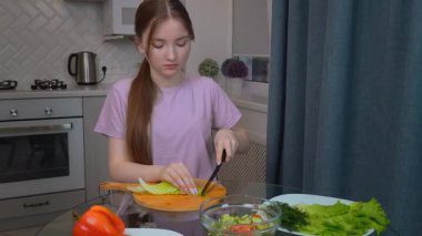 Genç kız marul yapraklarını düzgünce doğradı ve cam masanın üzerinde Çin lahanası hazırladı, renkli sebzelerle taze, besleyici bir salata hazırladı.