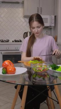 Genç kız marul yapraklarını düzgünce doğradı ve cam masanın üzerinde Çin lahanası hazırladı, renkli sebzelerle taze, besleyici bir salata hazırladı.