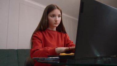 Genç kız öğrenci, çalışkan öğrenci, ev mutfağında dizüstü bilgisayar çalışıyor, etrafı kitaplarla çevrili, kasıtlı çalışmalar ve akademik uğraşlar gösteriyor.