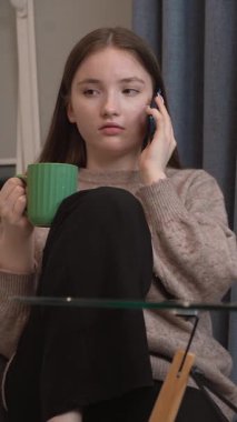 Genç kız dinleniyor, akıllı telefonla sohbet ediyor, sosyal medya uygulamalarına kayıyor, arkadaşlarına mesaj atıyor, ev ortamında rahat bir videoda çevrimiçi videolar izliyor.