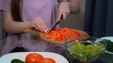 Profesyonel aşçı manikürlü. Tahta kesme tahtasına kırmızı dolma biberi dikkatlice dilimler. Taze sebzeleri sağlıklı ve besleyici yemekler için özel pişirme tekniğiyle hazırlar.