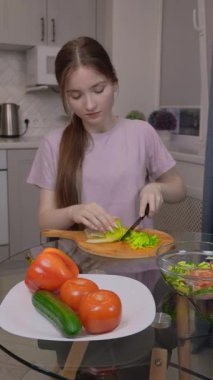 Genç kız marul yapraklarını düzgünce doğradı ve cam masanın üzerinde Çin lahanası hazırladı, renkli sebzelerle taze, besleyici bir salata hazırladı.