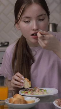 Ergen kız portakal suyunu yudumlarken besleyici salata yiyor ve yatay mutfak masasında rahat bir sabah yemeği yerken akıllı telefonlara bakıyor.