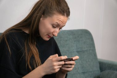 Genç bir kadın rahat bir koltukta oturuyor, akıllı telefonunu internet ve sosyal medyada gezinmek için kullanıyor, bağlantı ve modern teknolojinin tadını çıkarıyor.