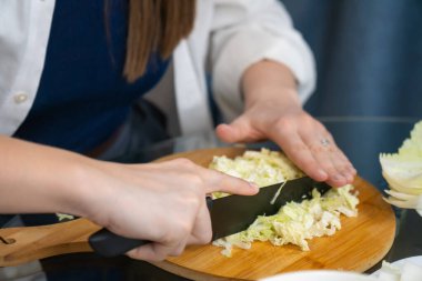 Ahşap kesim tahtasında taze Pekin lahanası dilimleyen kadın şef, profesyonel bir mutfak ortamında sağlıklı bir yemek için gerekli malzemeleri hazırlıyor.