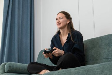 Genç bir kadın oturma odasındaki canlı yeşil bir kanepede rahat bir şekilde oturuyor, elinde bir oyun sahası tutuyor ve video oyunlarına dalmış, boş zamanlarının tadını çıkarıyor ve her anın tadını çıkarıyor.