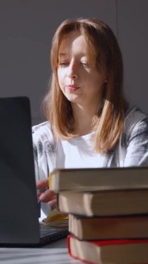 Düşünceli bir kadın ev ofis ortamında, kitap ve gözlüklerle uzaktan kumandayla çalışıyor. Odaklanmış konsantrasyon ve problem çözen dikey videolar öneriyor.