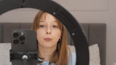 Genç kadın nüfuzlu biri, yandaşlarına cep telefonu ve zil ışığı kullanarak makyaj dersi verirken ruj sürüyor.