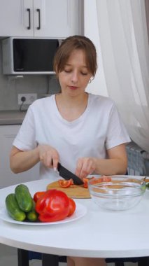 Keskin bir bıçakla domates doğrayan ve modern bir mutfakta sebze salatası hazırlayan bir kadının yakın çekimi. Sağlıklı yemek, ev yemeği, yemek pişirmeyi simgeliyor.,