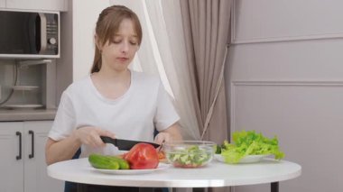 Keskin bir bıçakla domates doğrayan ve modern bir mutfakta sebze salatası hazırlayan bir kadının yakın çekimi. Sağlıklı yemek, ev yemeği, yemek pişirmeyi simgeliyor.,