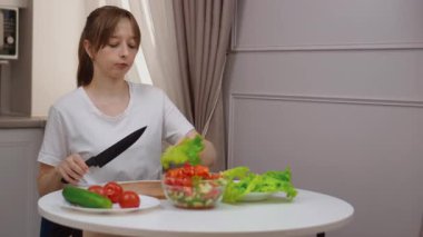 Profesyonel kadın aşçı, kırsal ahşap kesim tahtasının üzerinde gevrek yeşil marulu dikkatlice dilimliyor. Besleyici ev yapımı yemekler için hassasiyetle ve aşçılık uzmanlığıyla taze malzemeler hazırlıyor.