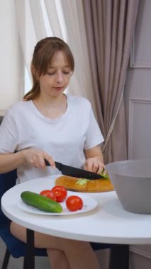 Profesyonel kadın aşçı, kırsal ahşap kesim tahtasının üzerinde gevrek yeşil marulu dikkatlice dilimliyor. Besleyici ev yapımı yemekler için hassasiyetle ve aşçılık uzmanlığıyla taze malzemeler hazırlıyor.