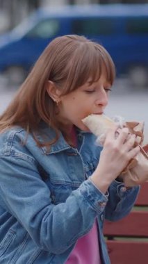 Güzel genç bir kadın ya da kız, işlek bir caddede bankta otururken lezzetli vejetaryen ya da vejetaryen kebap kebabı yiyor. Fast food ve abur cubur konsepti. Etik tüketim.