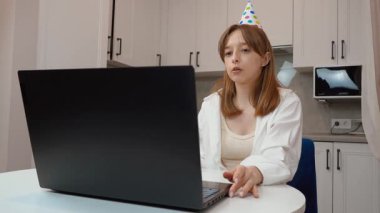 Parti şapkalı genç bir kadın doğum gününü pastadaki mumla kutluyor. Arkadaşları ve akrabalarıyla sohbet ediyor. Evde otururken bilgisayarla video görüşmesi yapıyor.