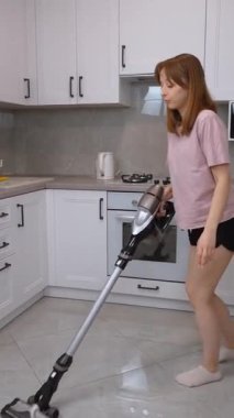 Kablosuz süpürgeyle neşe saçan ev hanımı, rutin mutfak temizliğini parlak, modern apartman içi dikey video içerisindeki eğlenceli ve enerjik dans performansına dönüştürüyor.