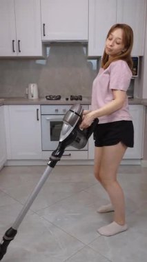 Kablosuz süpürgeyle neşe saçan ev hanımı, rutin mutfak temizliğini parlak, modern apartman içi dikey video içerisindeki eğlenceli ve enerjik dans performansına dönüştürüyor.