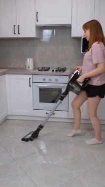 Kablosuz süpürgeyle neşe saçan ev hanımı, rutin mutfak temizliğini parlak, modern apartman içi dikey video içerisindeki eğlenceli ve enerjik dans performansına dönüştürüyor.