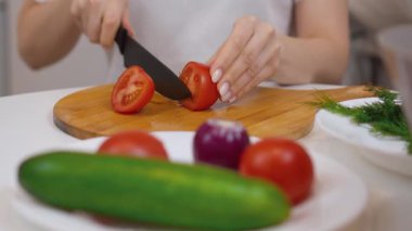 Kadın şef taze, olgun domatesleri ahşap bir kesim tahtasının üzerinde dilimler, salatalıklı, kırmızı soğanlı ve dereotlu sağlıklı ve renkli bir salata hazırlar