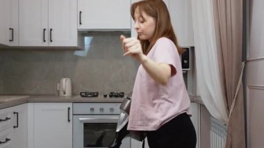 Evini temizlerken ya da ev işi yaparken müzik dinleyip dans eden pozitif bir genç kadın. Genç bir bayanla dans, mutluluk ve hijyen. Ev eşyaları ve ev eşyaları için.