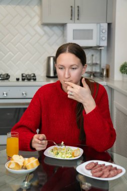 Genç bir kadın modern bir mutfakta besleyici ve lezzetli bir yemeğin tadını çıkarıyor, rahat atmosferin tadını çıkarıyor ve dengeli, sağlıklı bir diyet için taze malzemelerin tadını çıkarıyor. Dikey fotoğraf