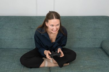 Rahat bir kanepede oturan genç bir kadın, elinde bir oyun platformu ile ve evinde video oyunları oynarken kızgın bir ifade sergiliyor.