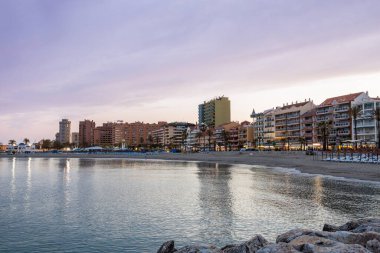 Sunset over the beach, calm Mediterranean Sea and Fuengirola city illuminated seafront with hotels. Fuengirola, Costa del Sol, Malaga province, Andalusia, Spain.