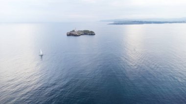 Suya yansıyan bulutlarla Cantabrian denizi, Faro de Mouro deniz feneri ve yelkenli. Sabah erkenden. Santander, Cantabria, İspanya.