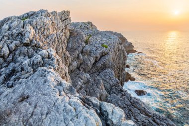 Kireçtaşı ve kumtaşı sahil kayalıkları, Cantabrian denizi ve gün batımı manzarası. Atlantik Okyanusu, Virgen del Mar Adası, Cantabria, İspanya.
