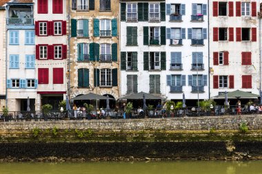 Renkli panjurlu geleneksel Fransız evleri, Nive nehri, toprak seti ve sokak kafelerinde dinlenen insanların manzarası. Bayonne, Pirenes-Atlantik, Fransa.