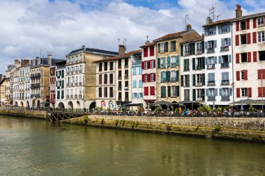 Renkli panjurlu geleneksel Fransız evleri, Nive nehri, toprak seti ve sokak kafelerinde dinlenen insanların manzarası. Bayonne, Pirenes-Atlantik, Fransa.