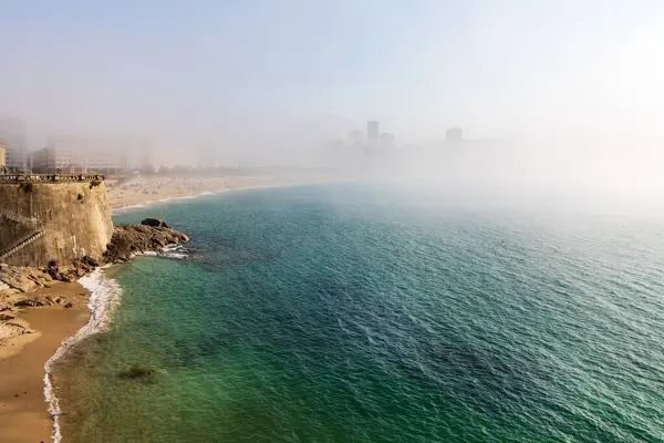 Güneşli bir günde yoğun sis. Atlantik Okyanusu, sahil, rıhtım ve sislerin içindeki şehir binaları. La Coruna, Galiçya, İspanya.