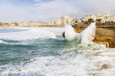 Şiddetli bir fırtınada kıyıdaki sarı kayaya çarpan bir dalga. Arka planda şehir binaları var. Biarritz, Pireneler-Atlantikler, Fransa.