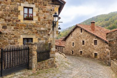 Kırsal dağ taşından evler ve kırmızı çatıları olan bir kaldırım taşı sokağının kıvrımları. Barcena Belediye Başkanı, Cantabria, İspanya.
