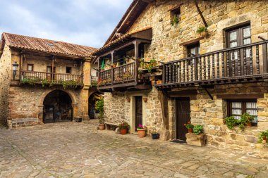 Çiçeklerle süslenmiş, ahşap balkonları ve küller kemerlerle açılmış atari salonlarıyla dolu eski dağ evleri olan bir cadde manzarası. Barcena Belediye Başkanı, Cantabria, İspanya.