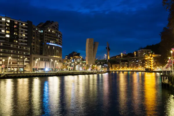 Aydınlatılmış Bilbao nehir kenarının akşam manzarası, Nervion Nehri 'ndeki ışıkların yansımaları, ve uzaktaki La Salve Köprüsü. Bilbao, Vizcaya, Bask Ülkesi, İspanya.
